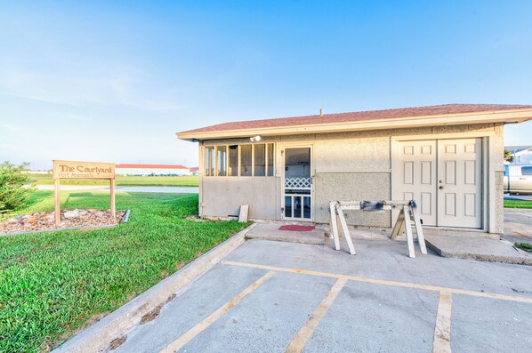 A small building with a sign reading "The Courtyard Port Aransas Tx." It has a single door and a small window, with a parking lot in front.