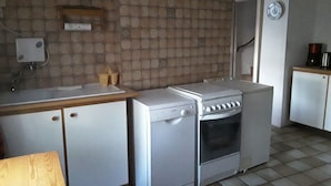 Eine kleine Küche mit Spüle, Herd und Geschirrspüler. Es gibt eine Holz Arbeitsplatte und einen kleinen Schrank.
