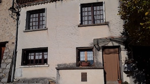 Ein zweigeschossiges Gebäude mit vielen Fenstern, einer Holztür und einer Steinwand.