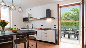 Eine moderne Küche mit Kochinsel, Gasherd und eingebautem Backofen. Durch einen offenen Durchgang ist eine Essecke mit Tisch und Stühlen erkennbar.