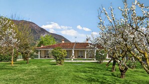 A house with a red-tiled roof, surrounded by a well-maintained lawn and flowering trees. - Regarda - "Villa Ida, Giarole unit" with pool and bisg garden (Costermano)