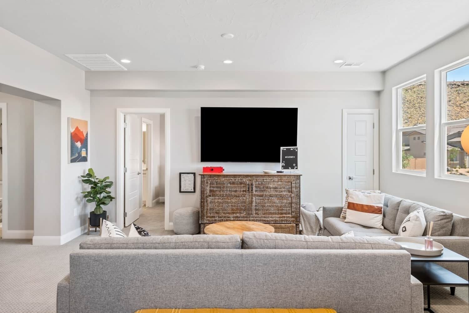 A modern living room with a large gray sectional sofa, a coffee table, and a flat-screen TV mounted on a textured wall.