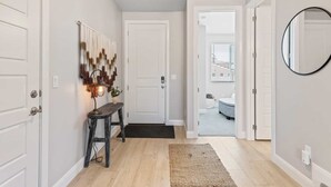 A hallway with a wooden floor, a bench, a wall-mounted lamp, and a door leading to a bathroom with a round mirror and a toilet. - Family Desert Oasis 5 Bedroom Home (Washington)