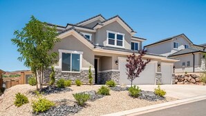 A two-story house with a stone facade, a garage, and a landscaped front yard with various plants. - Family Desert Oasis 5 Bedroom Home (Washington)
