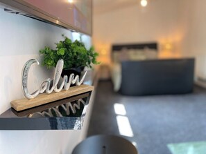 A modern interior with a decorative sign reading 'Calm' on a shelf, a potted plant, and a sofa in the background. - Cute+Cozy Guesthouse for 2 +secure offroad parking (Wolverhampton)