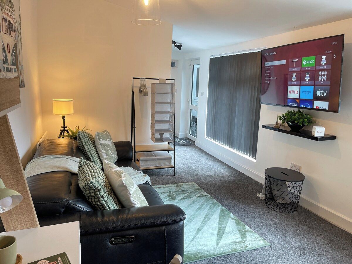 Ein modernes Wohnzimmer mit einer Ledersofa, einem stehenden Regal mit Dekoration, einem flachbildfernseher an der Wand und einer Treppe zu einem Balkon.