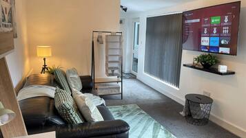 Ein modernes Wohnzimmer mit einer Ledersofa, einem stehenden Regal mit Dekoration, einem flachbildfernseher an der Wand und einer Treppe zu einem Balkon.