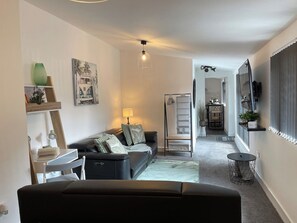 A modern living room with a sofa, a coffee table, and a lamp. There is a staircase leading to an upper level. - Cute+Cozy Guesthouse for 2 +secure offroad parking (Wolverhampton)