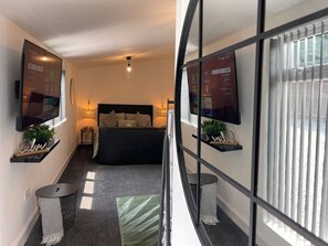 A modern bedroom with a bed, a TV, and a large window. - Cute+Cozy Guesthouse for 2 +secure offroad parking (Wolverhampton)