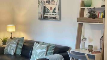A living room with a black leather sofa, a painting of a vintage car, a lamp, a bookshelf, and a small table.