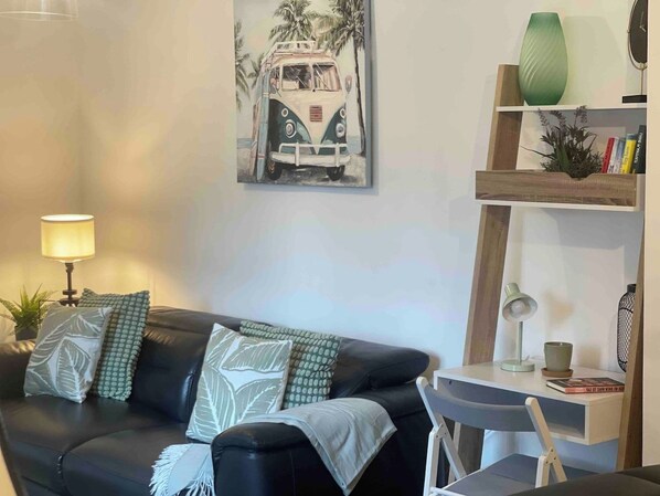 A living room with a black leather sofa, a painting of a vintage car, a lamp, a bookshelf, and a small table.