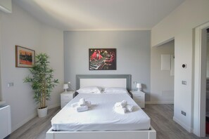 A modern hotel room with a large bed, two bedside tables, a potted plant, and artwork on the wall.