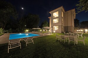 A modern two-story building with a swimming pool, outdoor seating, and a well-lit patio area.
