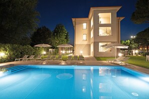 A modern two-story building with a swimming pool, outdoor seating, and well-lit surroundings.