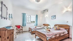 Ein Schlafzimmer mit zwei Holzbett, einem Holzschrank, einem Stuhl, einem Fenster mit Vorhängen und einer Wand-Klimaanlage.