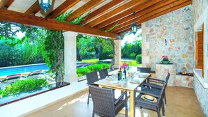 An outdoor patio with a stone wall, wooden ceiling, and a view of a swimming pool. - Villa Tanca - Three Bedroom Villa, Sleeps 6 (El Vilà)