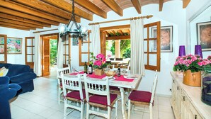 A dining area with a wooden ceiling, white table with red cushions, and a view of greenery outside. - Villa Tanca - Three Bedroom Villa, Sleeps 6 (El Vilà)