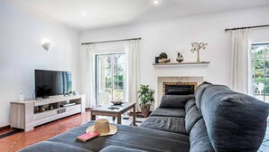 Ein modernes Wohnzimmer mit einem grauen Ecksofa, einem Flachbildfernseher, einem Kamin und einem großen Fenster mit Vorhängen.