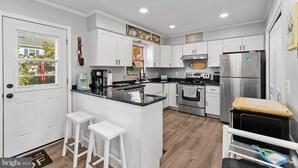 A modern kitchen with white cabinetry, a central island, and stainless steel appliances. - 4 bedroom, 2 bath home with covered deck, firepit, fenced yard - with linens! (Ocean View)