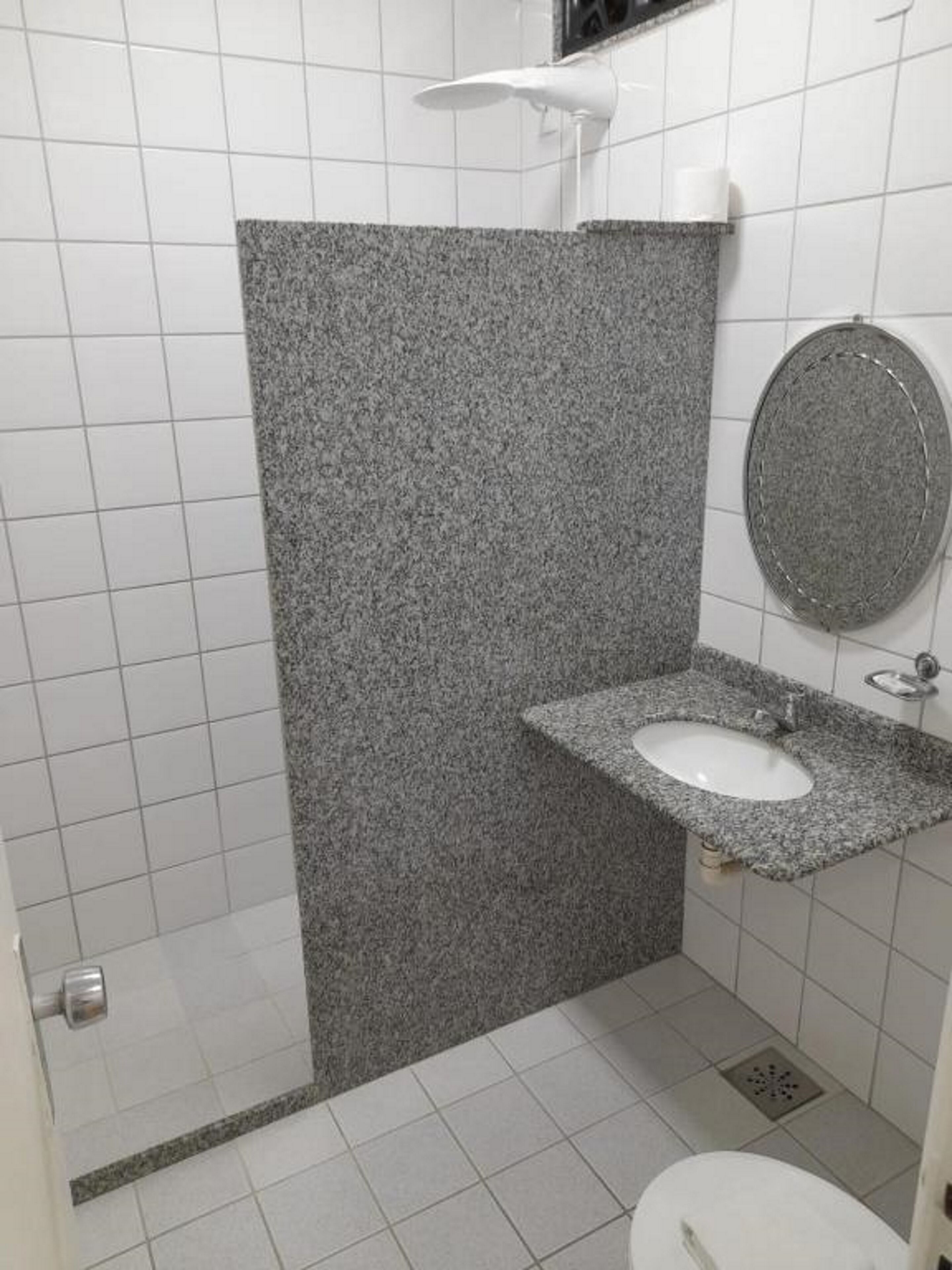 Casa de banho com lavatório branco, espelho e zona de duche.