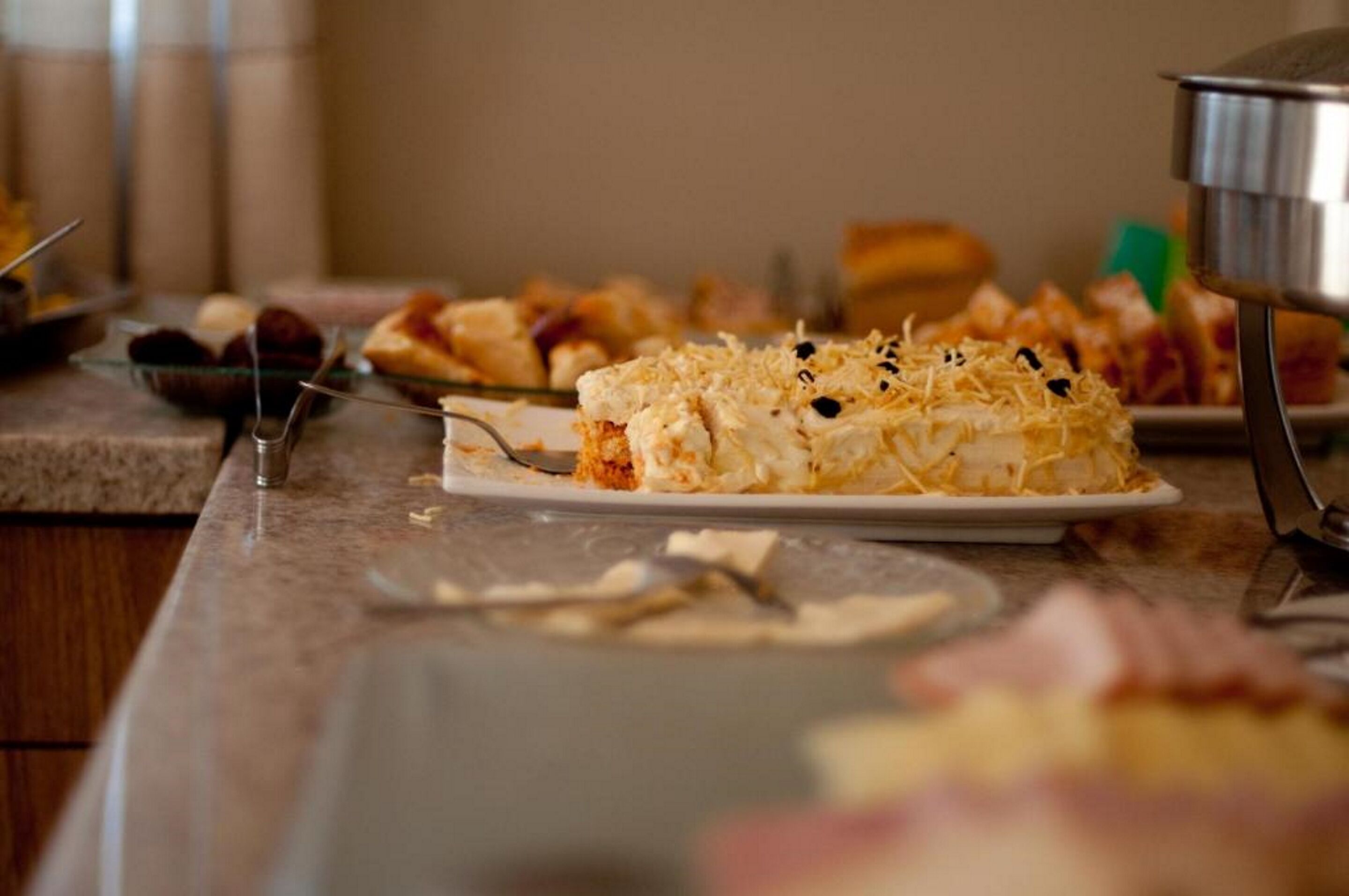 A buffet table with various dishes, including a large covered dish with shredded cheese and black seeds, and other food items in the background.