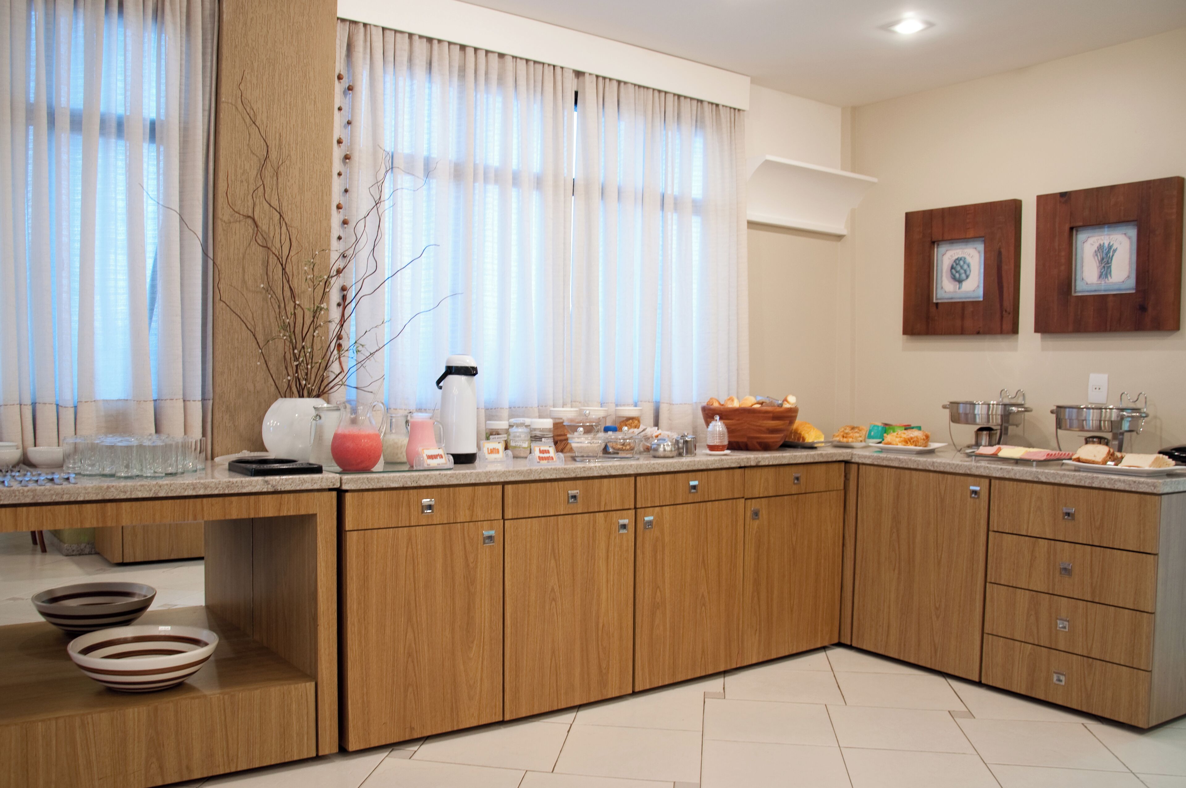 A modern kitchen with wooden cabinets, a countertop with various kitchen items, and a window with sheer curtains.