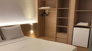 Un dormitorio con una cama grande, un armario, un refrigerador pequeño y una mesita de noche con una lámpara.