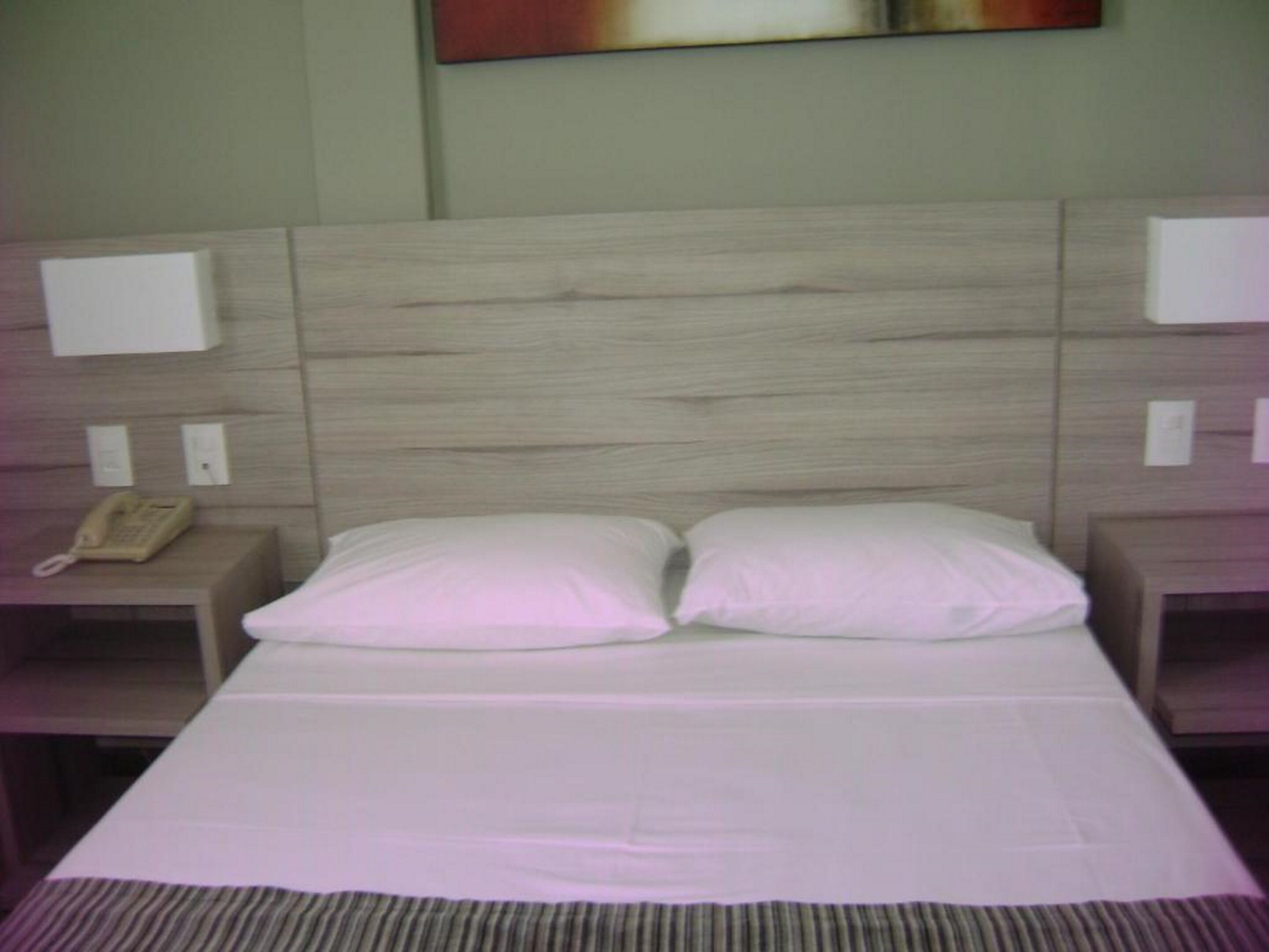 A hotel room with a wooden headboard, two white pillows, a striped rug, and a bedside telephone.