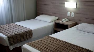 Quarto de hotel com duas camas, uma mesa de cabeceira com telefone e uma luminária na parede.