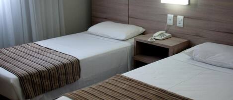 Habitación de hotel con dos camas, una mesita de noche con teléfono y una lámpara de pared.