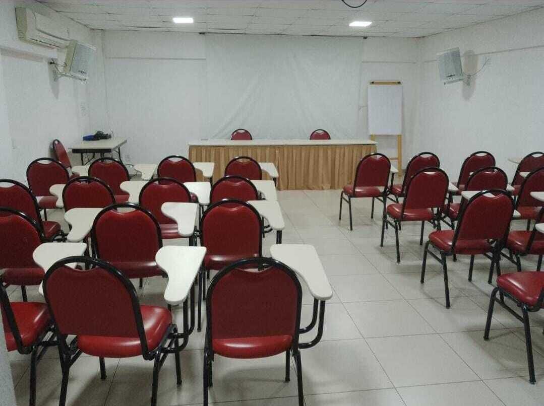 A conference room with rows of red chairs and white tables, a podium, and a whiteboard on the wall.