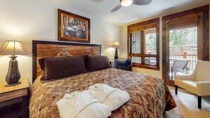 Ein Schlafzimmer mit einem großen Bett, einem Deckenventilator, einem Gemälde und Blick ins Freie durch ein Fenster.