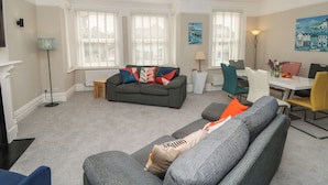 A living room with a grey sofa, a dining table with chairs, and a lamp.
