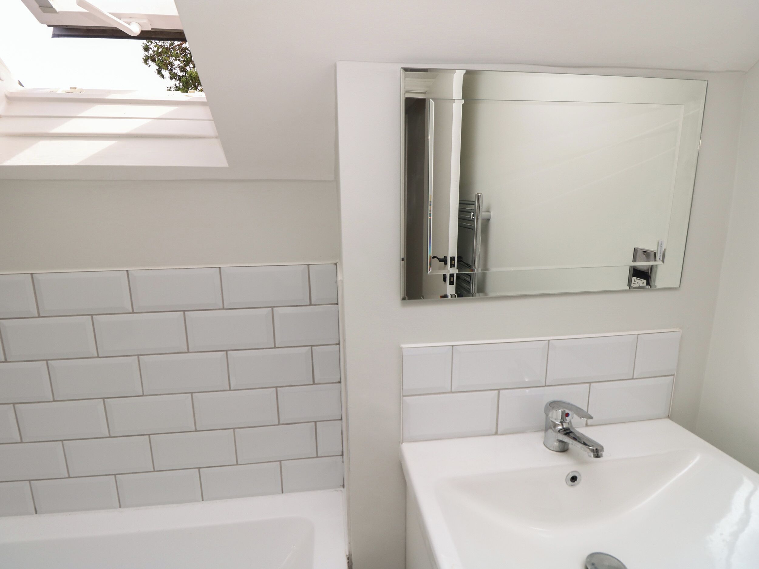Une salle de bain moderne avec des carreaux blancs, un grand miroir et un lavabo blanc.