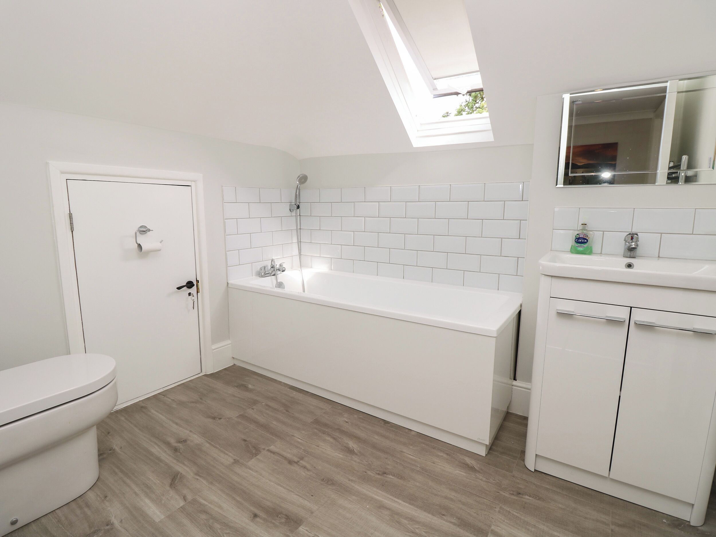 A modern bathroom with a white toilet, a freestanding bathtub, and a sink with a mirror above it.