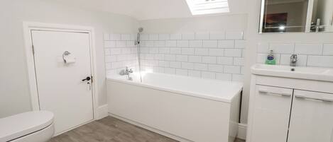 A modern bathroom with a white toilet, a freestanding bathtub, and a sink with a mirror above it.