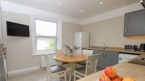 A compact kitchen with a dining area, a flat-screen TV mounted on the wall, and a window providing natural light.