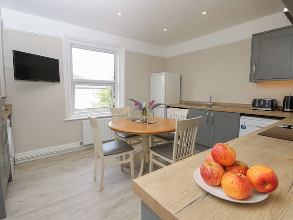 A compact kitchen with a dining area, a flat-screen TV mounted on the wall, and a window providing natural light.