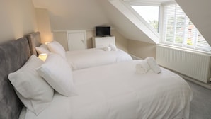 A bedroom with a sloped ceiling, a bed with white linens, a television on a nightstand, and a window with blinds.