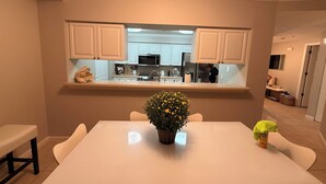 Une cuisine moderne avec des meubles blancs, un îlot central et un coin repas comprenant une table et des chaises.