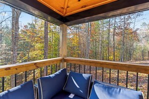 Eine Holzterrasse mit blauen, gepolsterten Sitzgelegenheiten und Blick auf einen Wald im Herbstlaub.