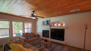 Una sala de estar acogedora con techo de madera, ventilador de techo, chimenea, televisor y sofá.