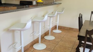 Una cocina con mostrador, taburetes blancos tipo bar, una mesa de comedor y sillas.