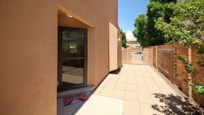 Un edificio con puerta de cristal, un patio empedrado y una valla adornada con plantas trepadoras.