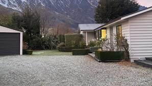 A house with a gravel driveway, a garage, and a well-maintained garden with hedges and bushes. - Frankton Favourite - Queenstown Holiday Home (Queenstown)