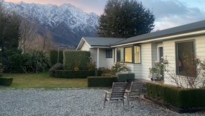 A house with a gravel driveway, two wooden chairs, and a view of snow-capped mountains. - Frankton Favourite - Queenstown Holiday Home (Queenstown)
