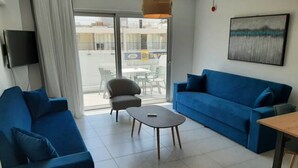 Un soggiorno moderno con un divano blu, un tavolino rotondo e una TV a parete.
