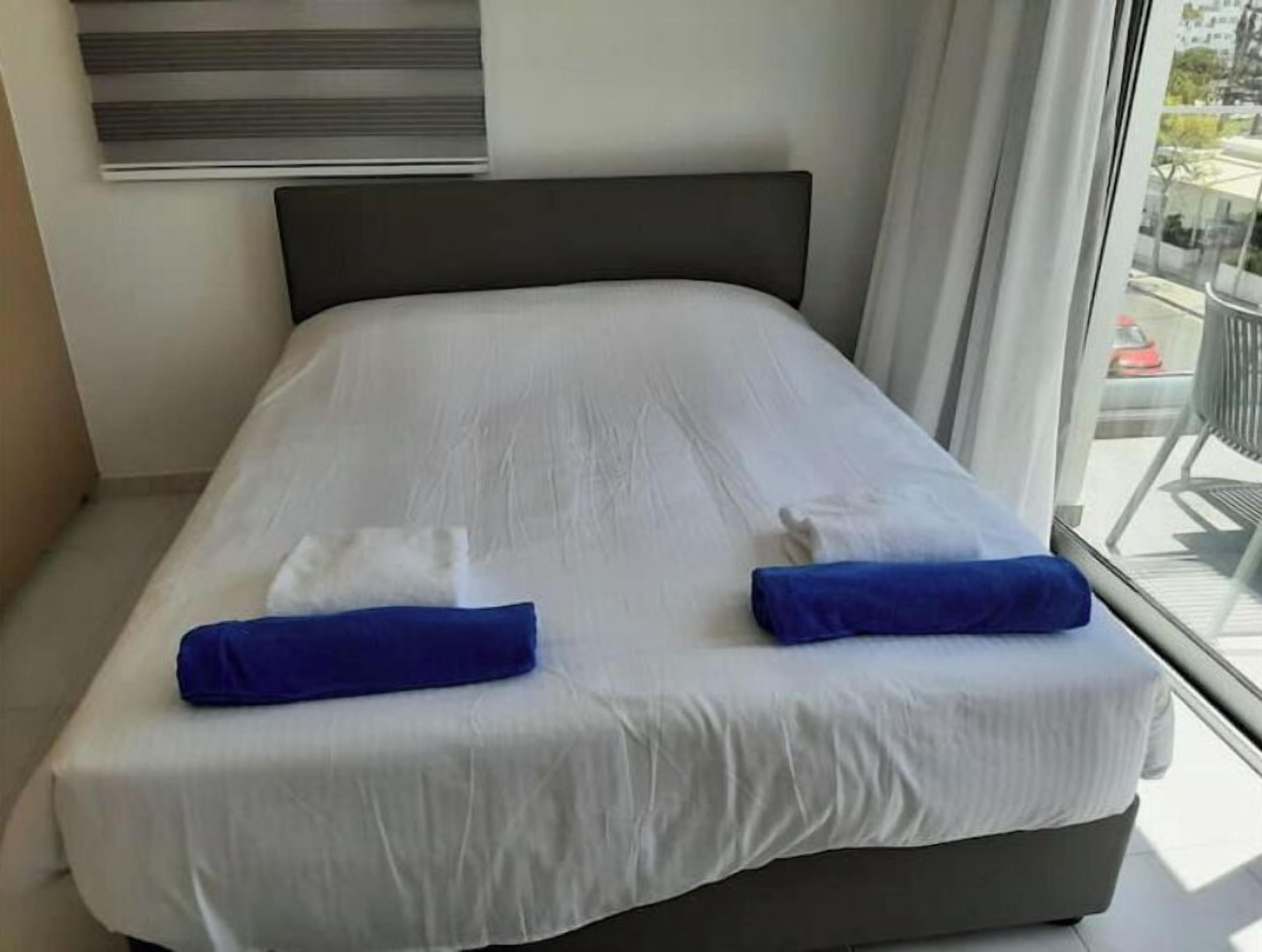 A modern hotel room with a large bed, white linens, and two blue towels.