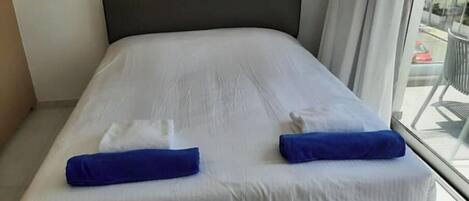 A modern hotel room with a large bed, white linens, and two blue towels.