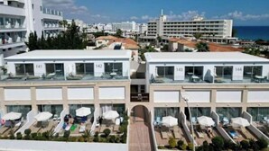Un hotel con balcones numerados, mobiliario exterior y vista al mar.